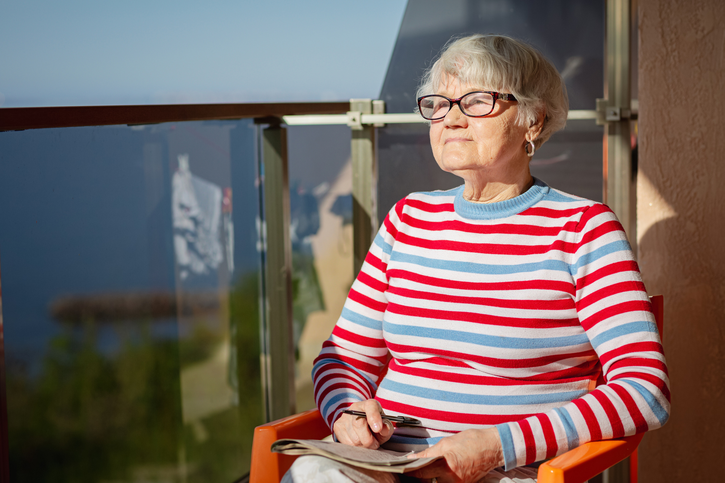 Elderly woman in glasses sitting on balcony near the sea